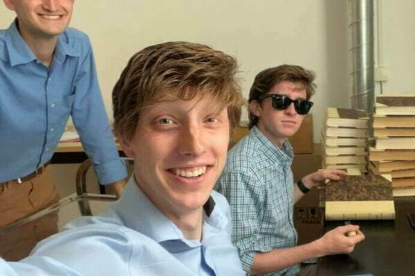 Three undergraduate men in coordinating blue button-down shirts pause from their work in the archives for a selfie.