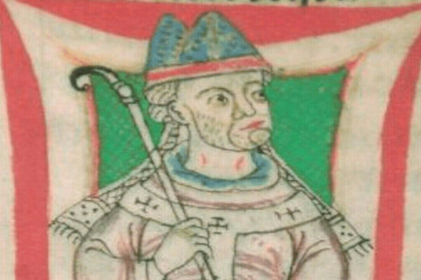 Medieval illumination of a bearded cleric wearing a blue and red mitre, a white robe with cross symbols, and a blue collar. He holds a silver crozier against a green background with red and white borders.